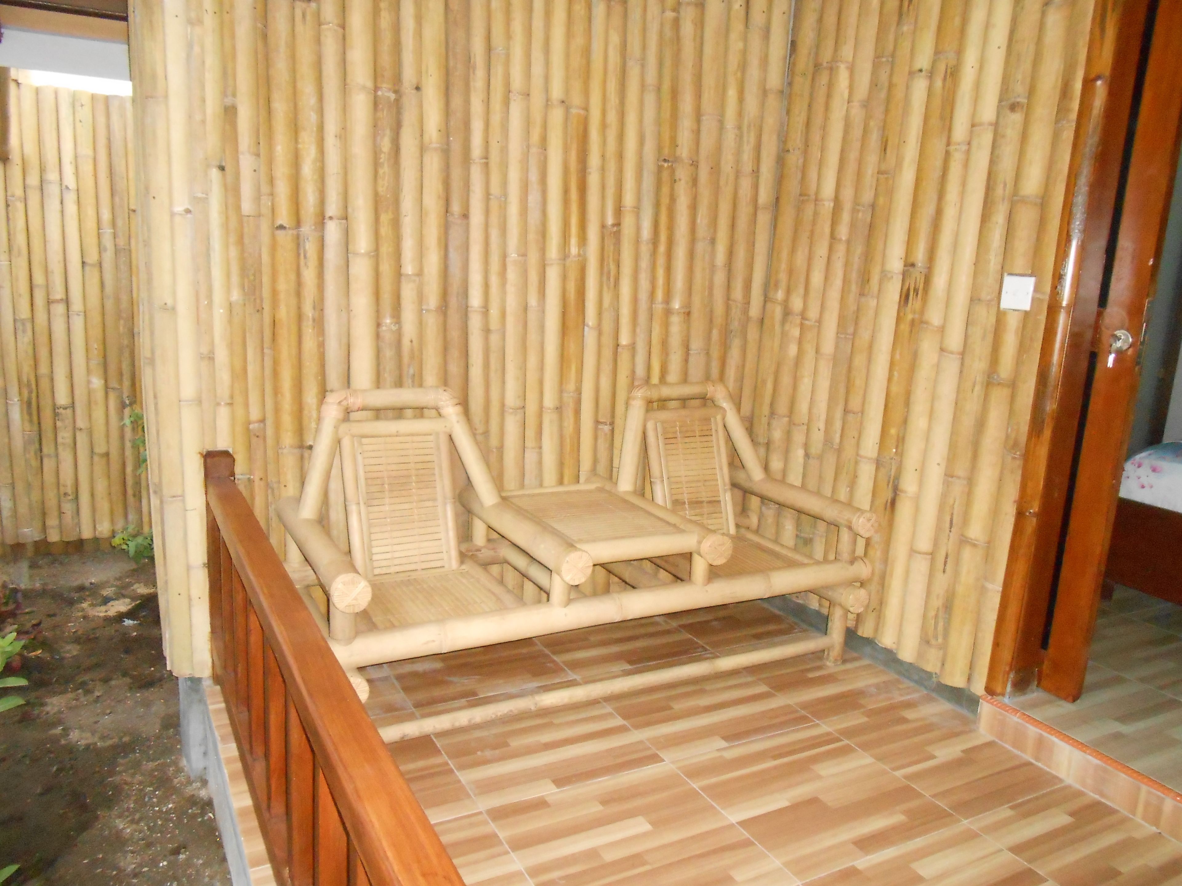 A room with a bamboo wall, two wooden chairs, a small table, and a wooden floor.