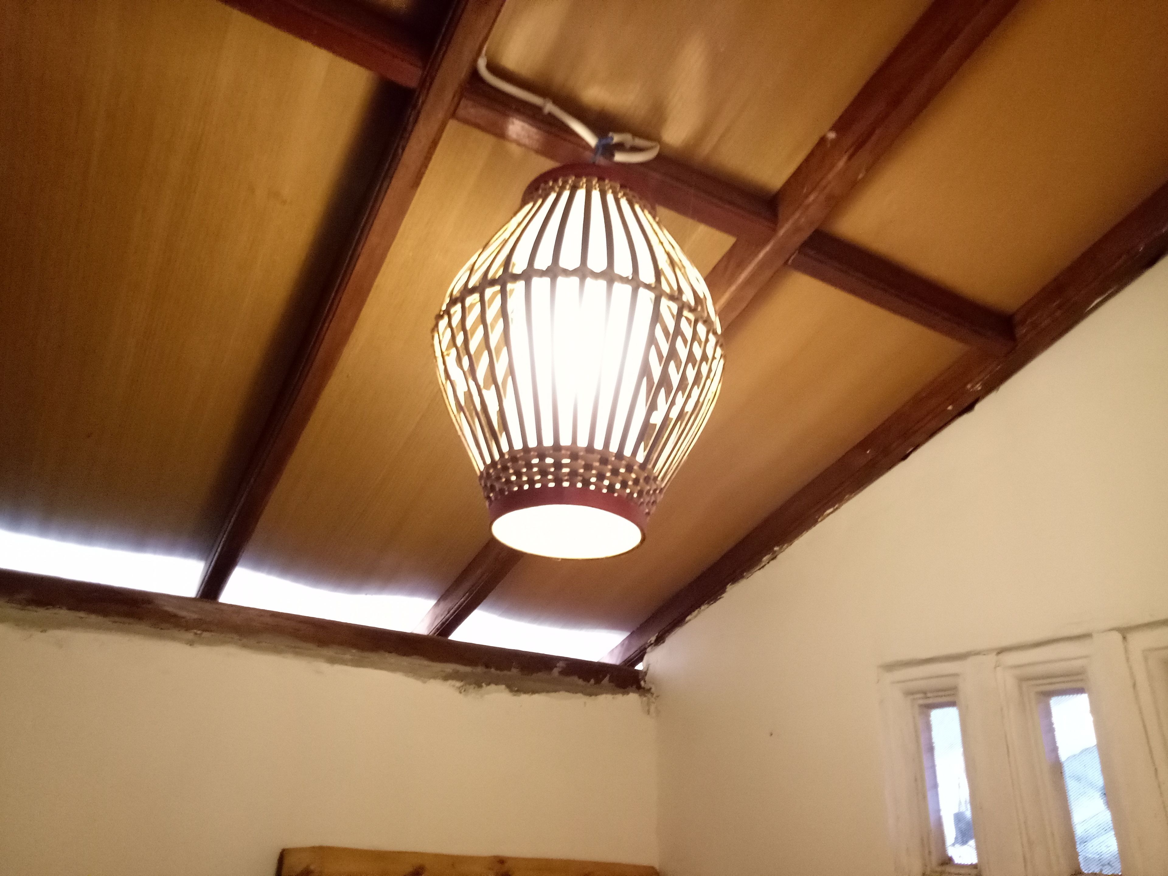 A room with a sloped ceiling, wooden beams, a hanging light fixture, and a window.