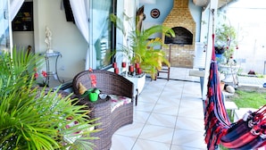 A covered patio area with a wicker sofa, potted plants, a hammock, and a brick oven. - Pousada Âncora de Ouro (Cabo Frio)