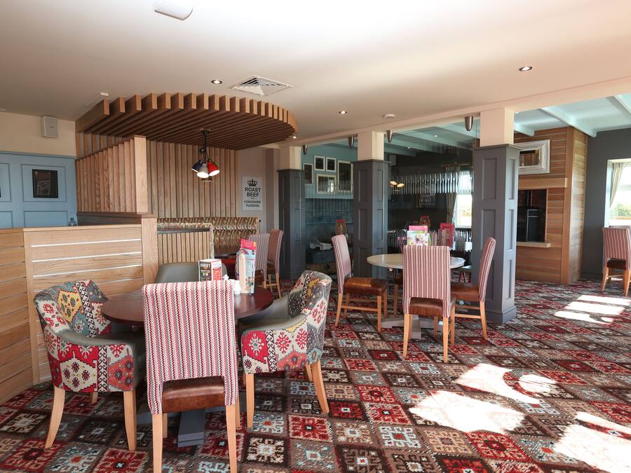 Un restaurante con alfombra estampada, mobiliario de madera y paredes en tonos azules y grises.