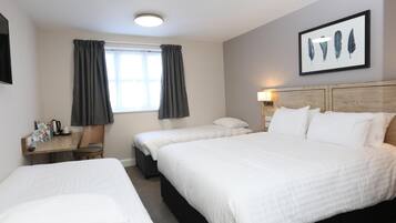 Una habitación de hotel con dos camas, un escritorio con silla, una ventana con cortinas, un cuadro en la pared y una mesita de noche con lámpara.