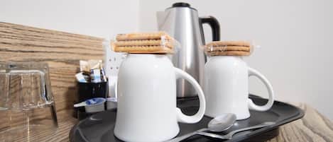 Two white mugs with a sandwich on top, a black tray with a spoon, and a silver coffee pot on a wooden table.