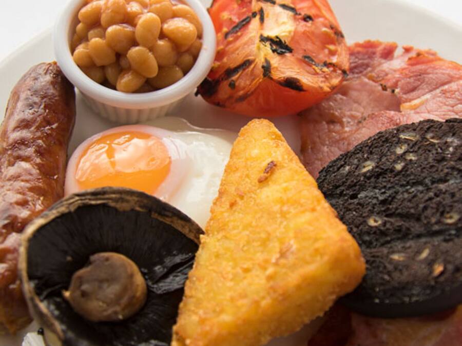 A plate with various foods including sausages, beans, a grilled tomato, a fried egg, mushrooms, and a slice of bread.