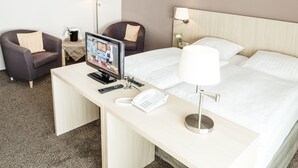 Habitación de hotel con cama, escritorio, televisor, silla, lámpara y teléfono.