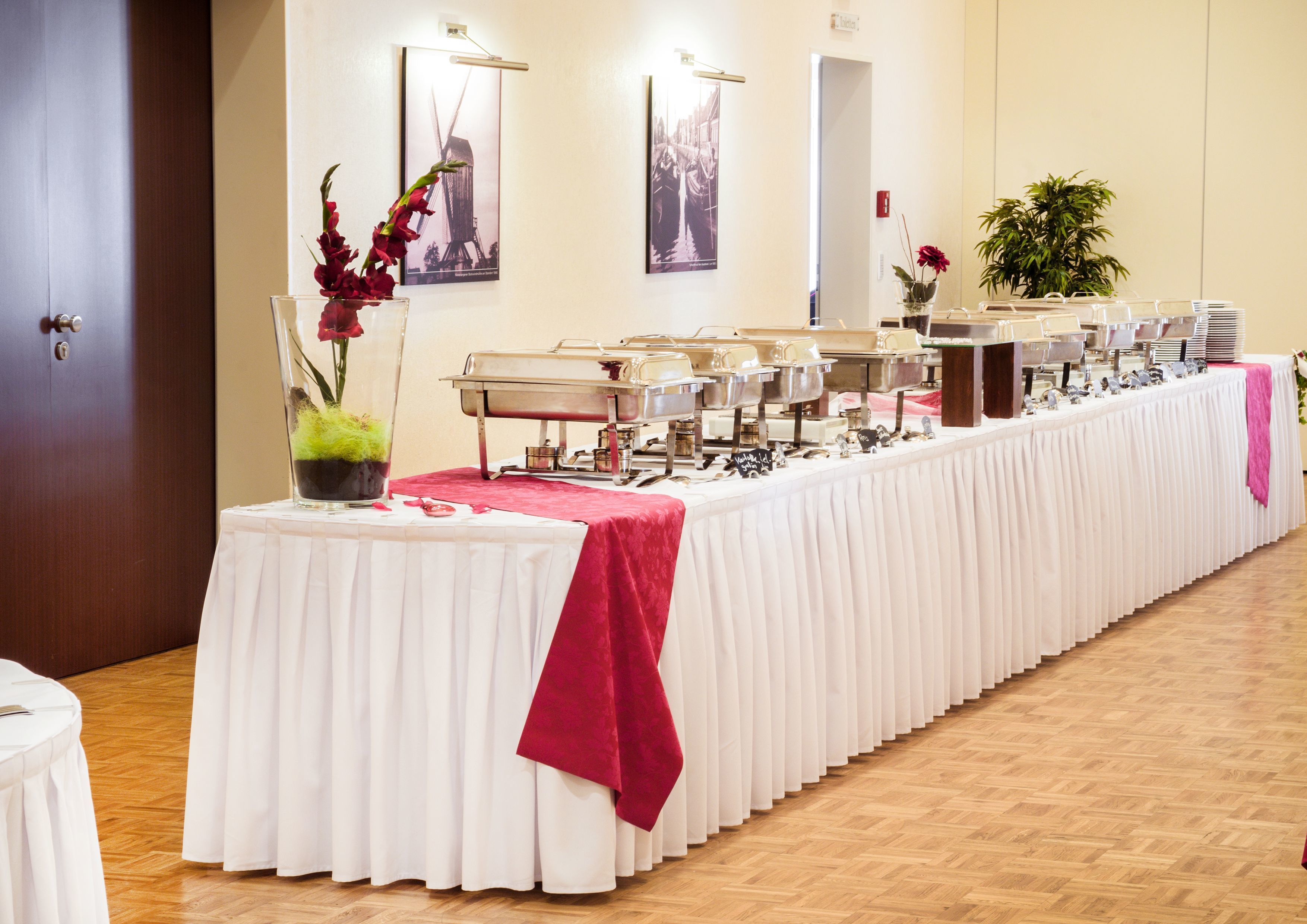 A buffet setup with multiple serving stations, a white tablecloth, and a red cloth draped over the table.
