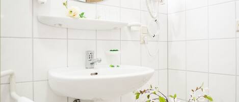 Un baño con lavamanos blanco, espejo, secador de pelo y toallero.