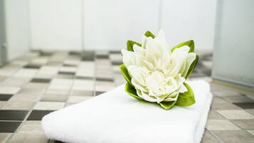 Une serviette blanche ornée d’une fleur blanche, posée sur un sol carrelé.