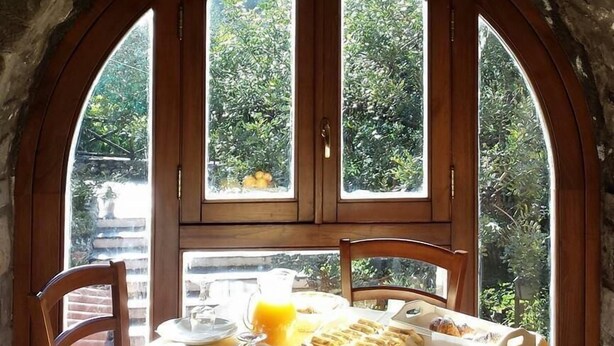 A breakfast table set in a stone-walled room with a large arched window overlooking a garden. - Nonno Luigino (Vico Equense)