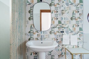 Un bagno con un lavandino bianco, uno specchio e piastrelle decorate con un motivo geometrico.