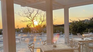 An outdoor patio area with tables and chairs, a view of the sunset, and a tree in the background. - Nonno Luigino (Vico Equense)