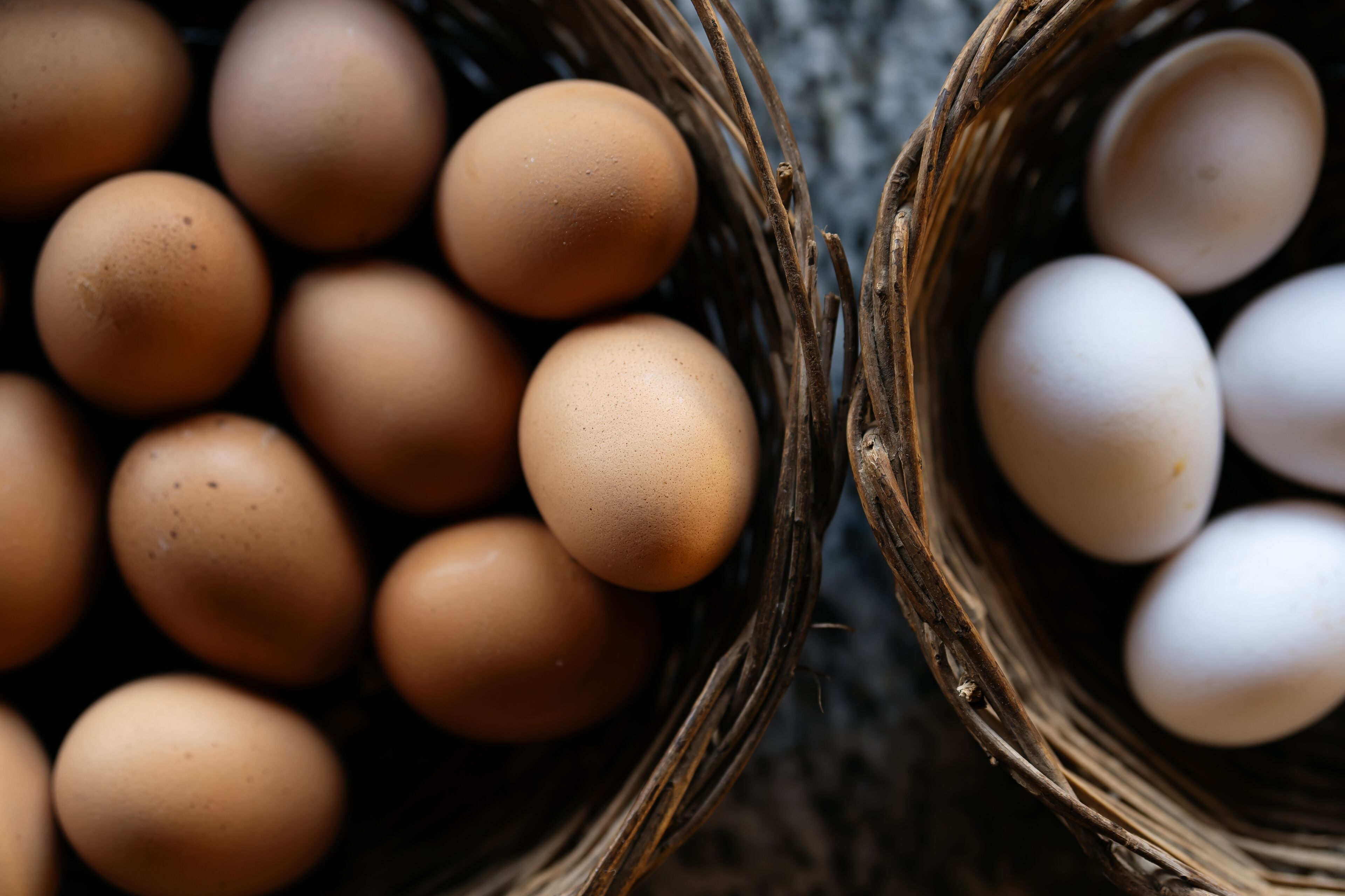 Two baskets filled with eggs, one with brown eggs and the other with white eggs.