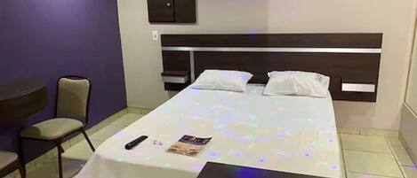Un dormitorio ordenado con cama, mesitas de noche, una silla y una pequeña mesa.