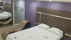 A hotel room with a bed, a chair, a mirror, and a small table.