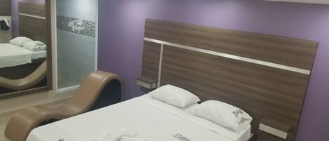 A hotel room with a bed, a chair, a mirror, and a small table.