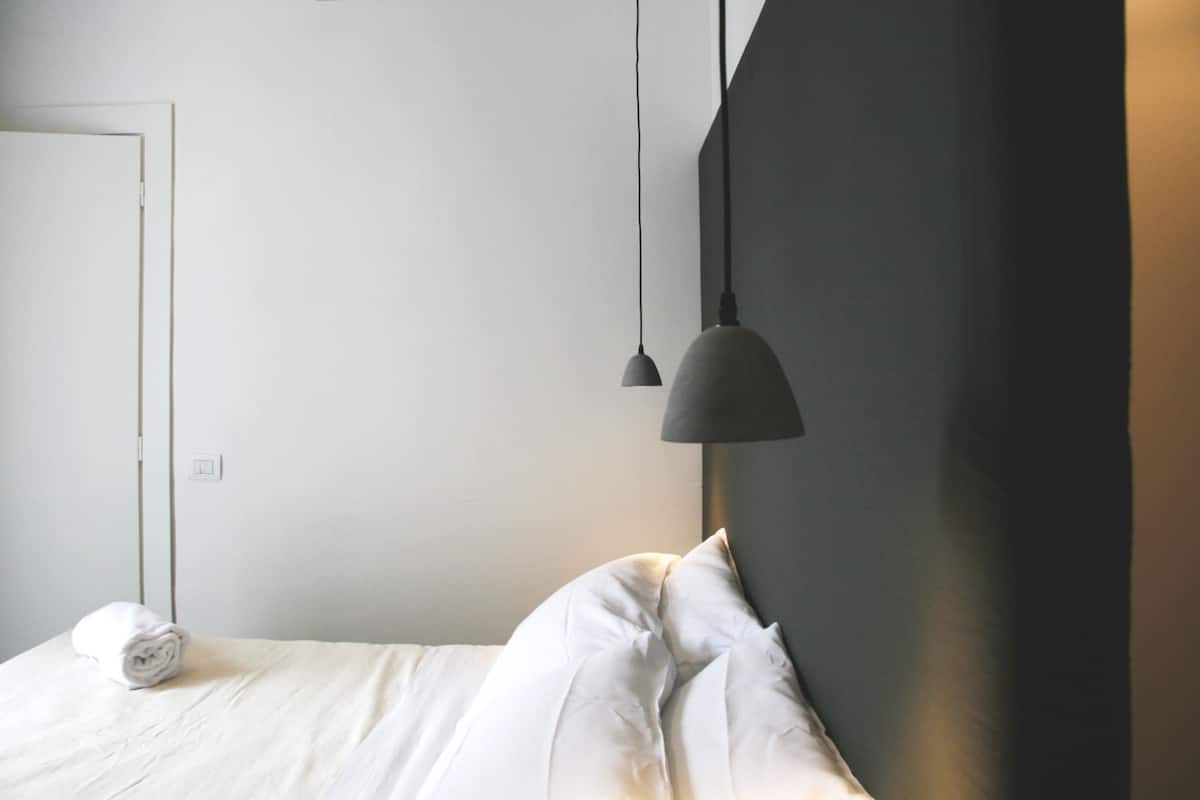 A bedroom with a bed, a white wall, a door, and a pendant light.