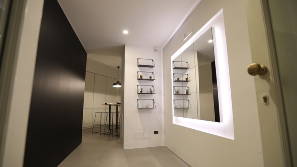A hallway with a black accent wall, a mirrored wall with shelves, and a dining area with a table and chairs. - The Station Napoli (Naples)