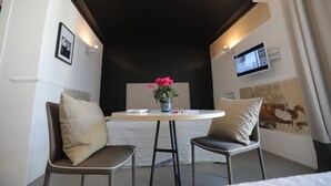 A small, modern room with a round table, two chairs, a vase with flowers, a television on the wall, and a unique black archway. - The Station Napoli (Naples)