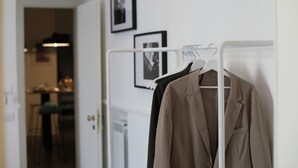 A clothing rack with a beige jacket and a black garment. There are framed pictures on the wall. - The Station Napoli (Naples)