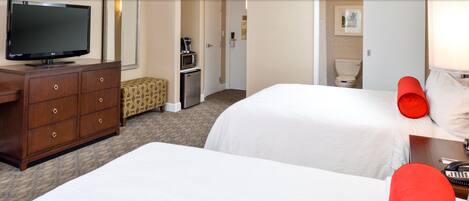 A hotel room with two beds, a television, a coffee maker, and a bathroom visible through an open door.