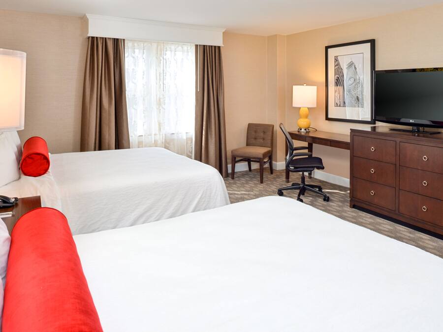 A hotel room with two beds, a desk with a chair, a television, and a dresser.