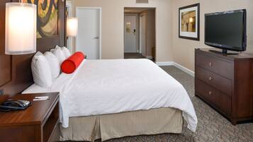 A hotel room with a large bed, a wooden dresser, a television, and a desk with a telephone.
