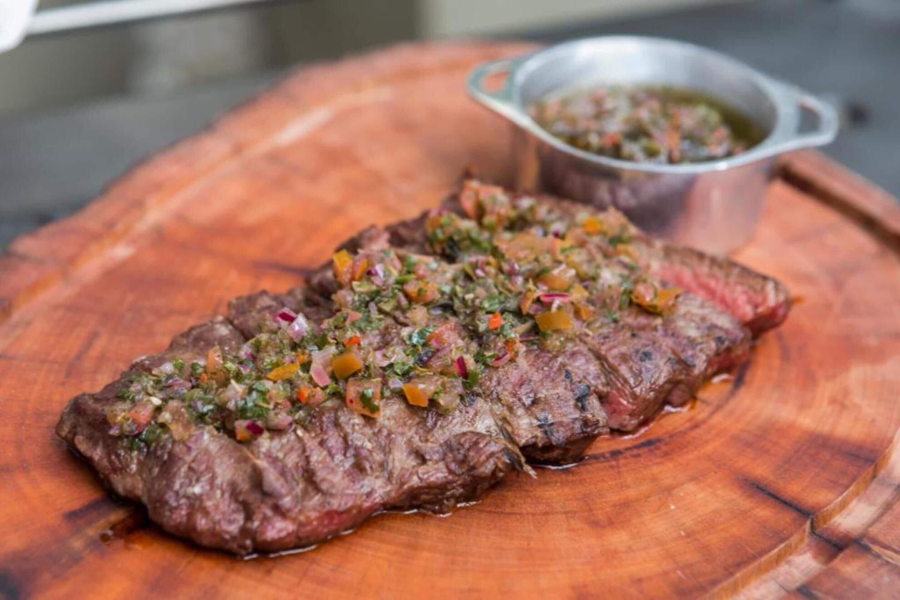 Bife com cobertura de ervas verdes sobre tábua de madeira.