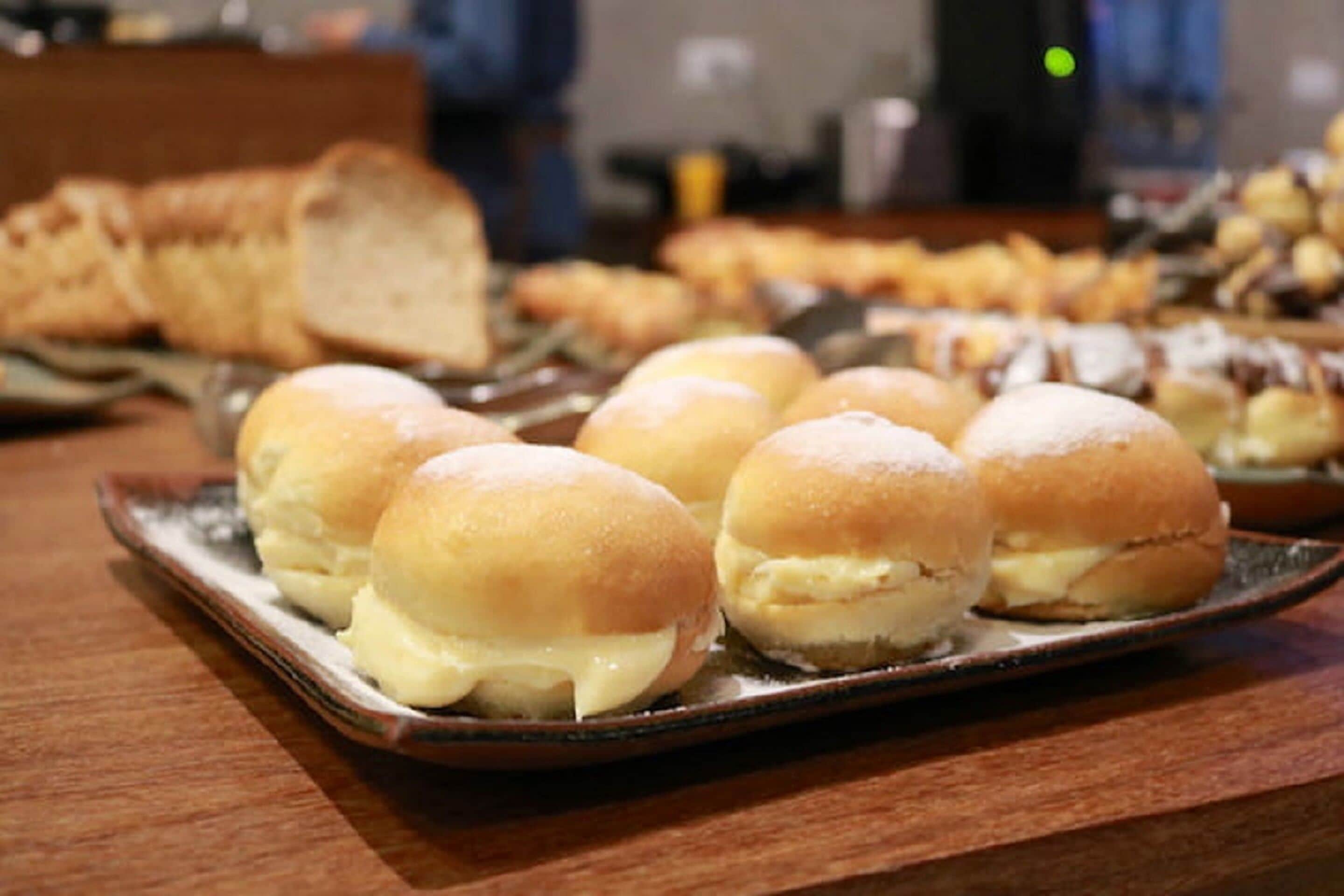 A tray of cream-filled buns on a wooden table.