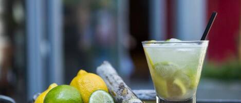 Un vaso de bebida helada con rodajas de lima y una pajita, acompañado de limas enteras y cortadas, y un trozo de jengibre sobre una superficie de madera.