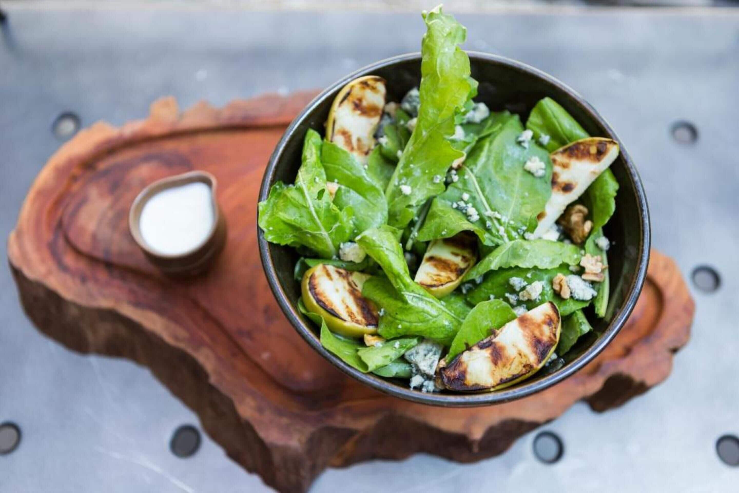 A salad bowl on a wooden board with a small bowl of dressing.