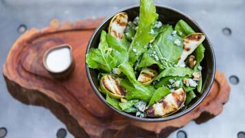 A salad bowl on a wooden board with a small bowl of dressing.