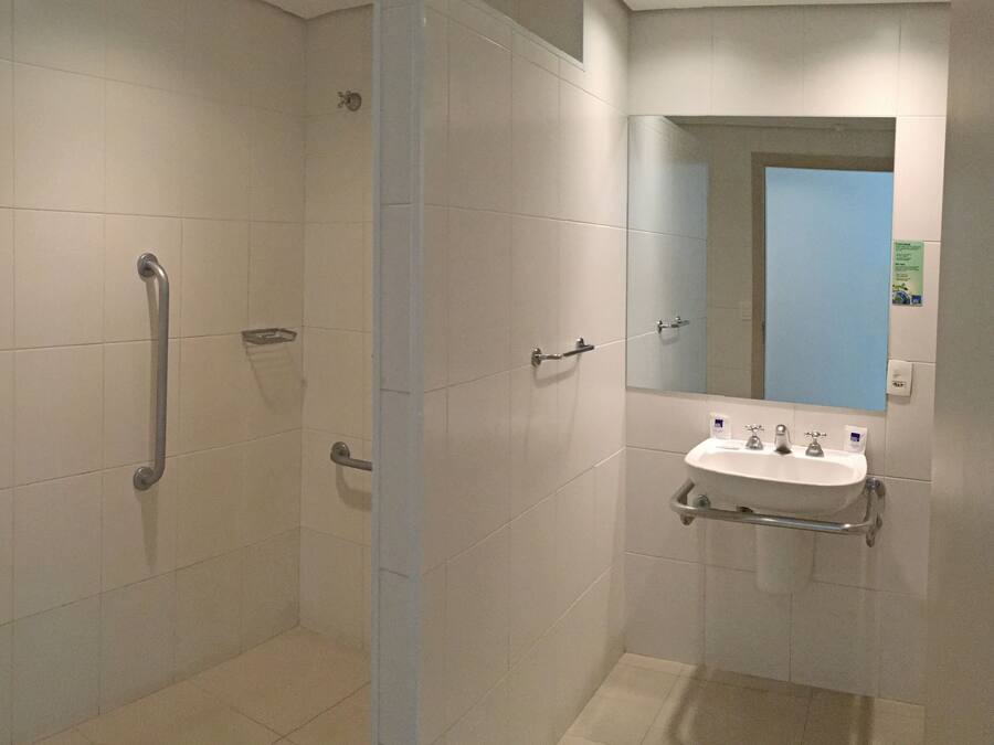 Un baño moderno con cabina de ducha, barras de apoyo, lavamanos con espejo y toallero.