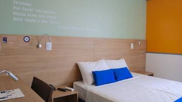 Une chambre d’hôtel avec un lit, un bureau et un mur orné d’une citation en portugais.