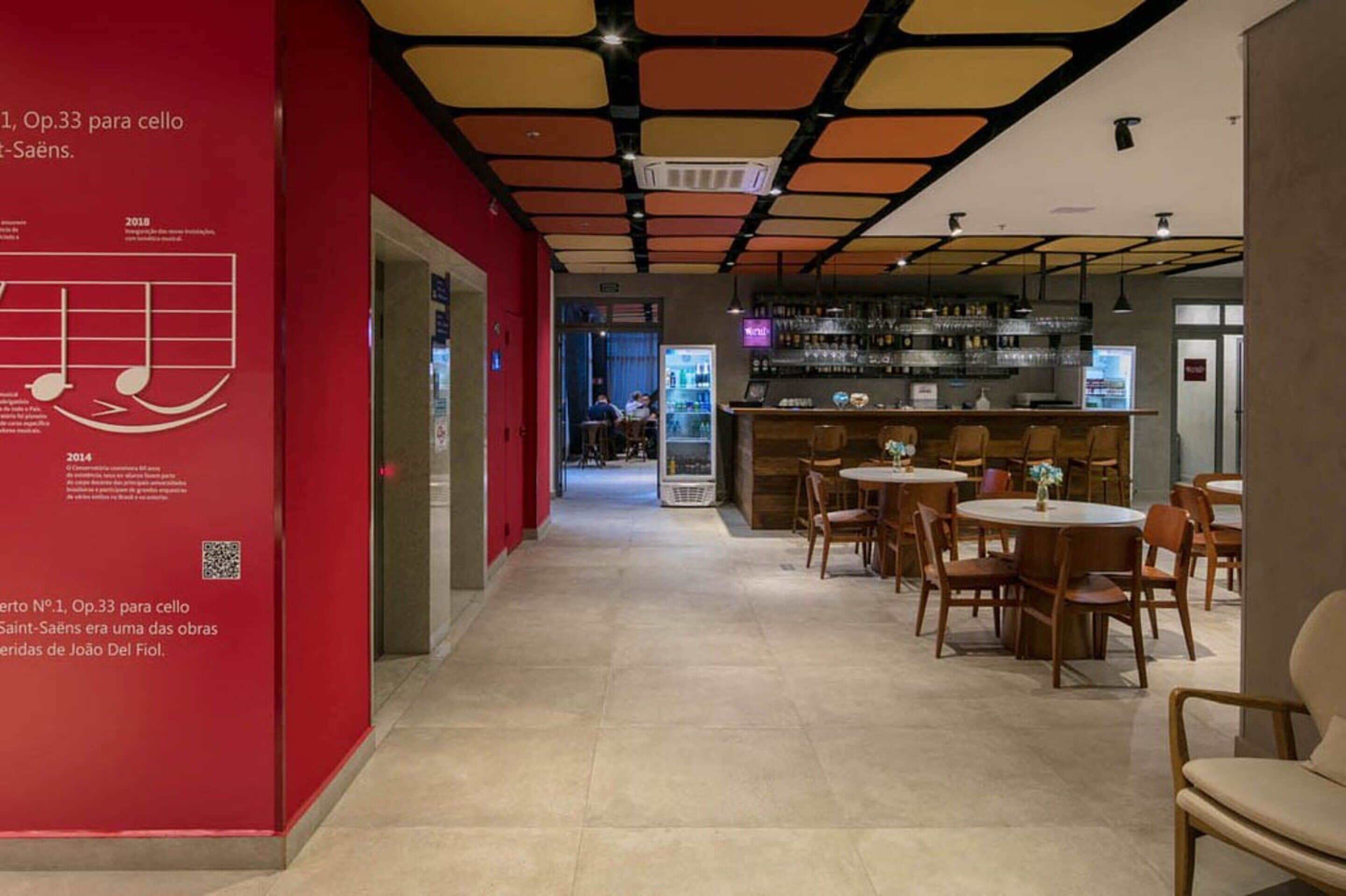 Um interior moderno com uma parede vermelha exibindo um código QR e texto, uma área de bar com banquetas e mesas com cadeiras.