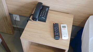 A wooden nightstand with a black telephone and a white remote control.