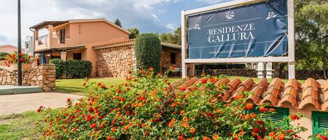 Un cartel que dice 'RESIDENZE GALLURA', con un edificio de piedra y un jardín al fondo.