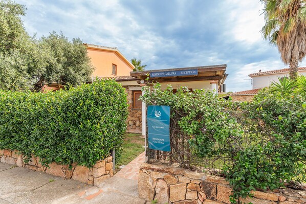 A reception area with a stone wall, a sign for 'RESIDENZE GALLURA', and a 'SEA TRAVEL' sign. - Residenze Gallura (San Teodoro)
