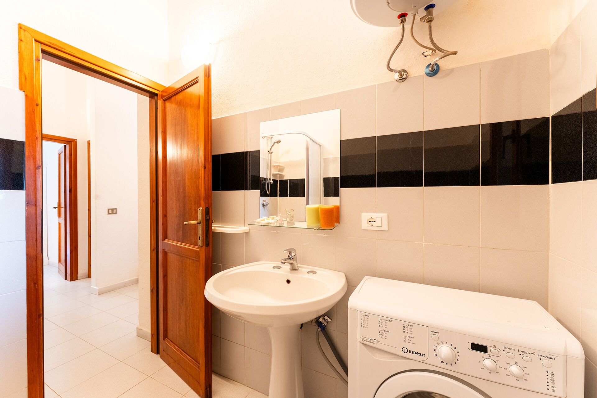 Un baño con puerta de madera, lavamanos, espejo, ducha y lavadora.