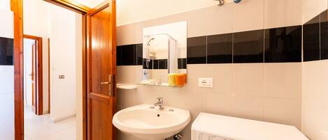 Un baño con puerta de madera, lavamanos, espejo, ducha y lavadora.