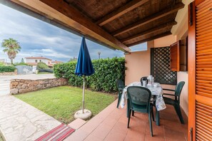 An outdoor patio with a table and chairs, a blue umbrella, and a stone wall. - Residenze Gallura (San Teodoro)