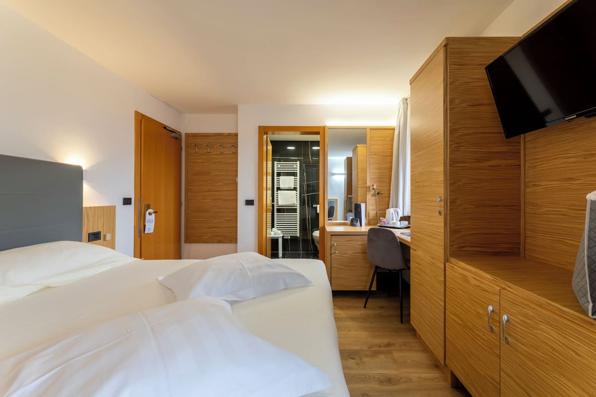 A hotel room with a bed, a desk, a chair, a TV, and wooden cabinets.