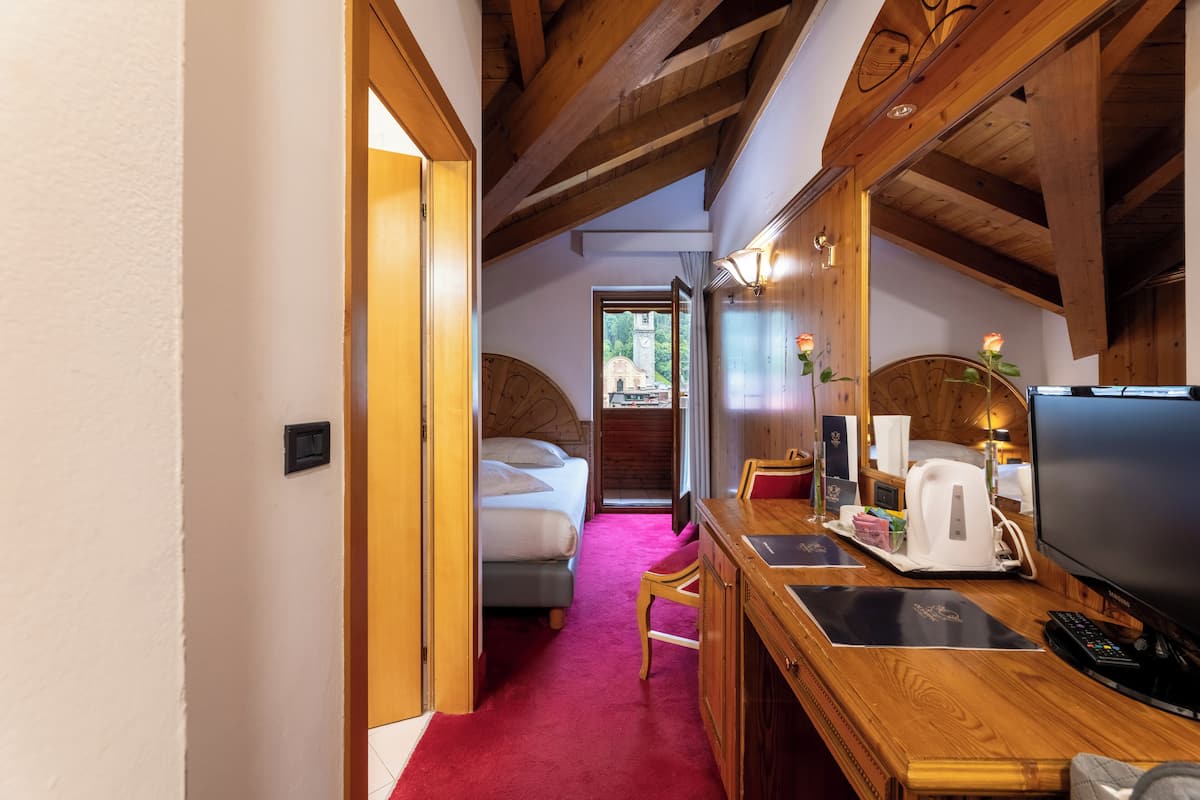 A hotel room with a wooden ceiling, a bed with a headboard, a desk with a television, and a red carpet.