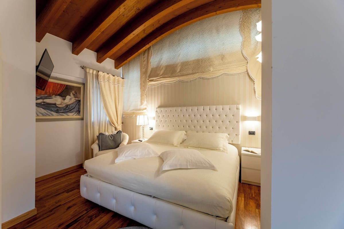 A bedroom with a large bed, wooden floor, and a painting on the wall.