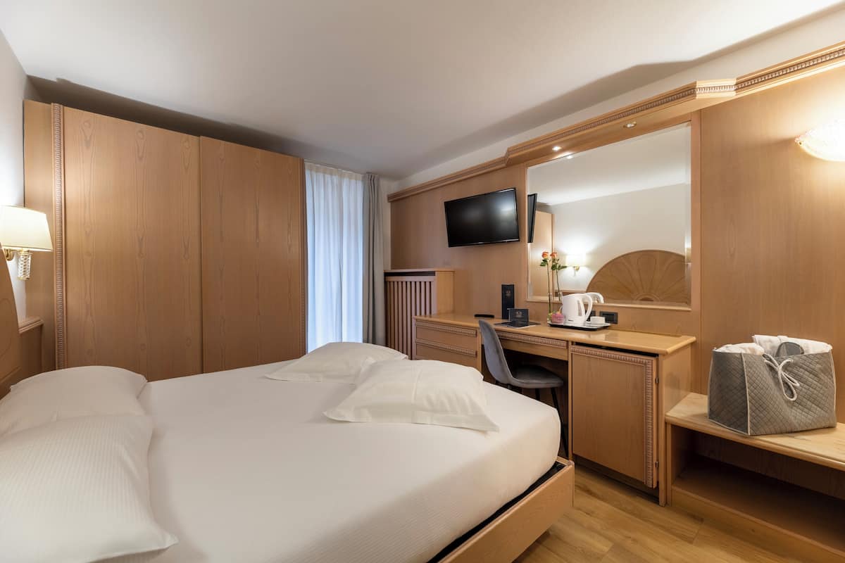 A hotel room with a large bed, a desk, a chair, a television, and a mirror.