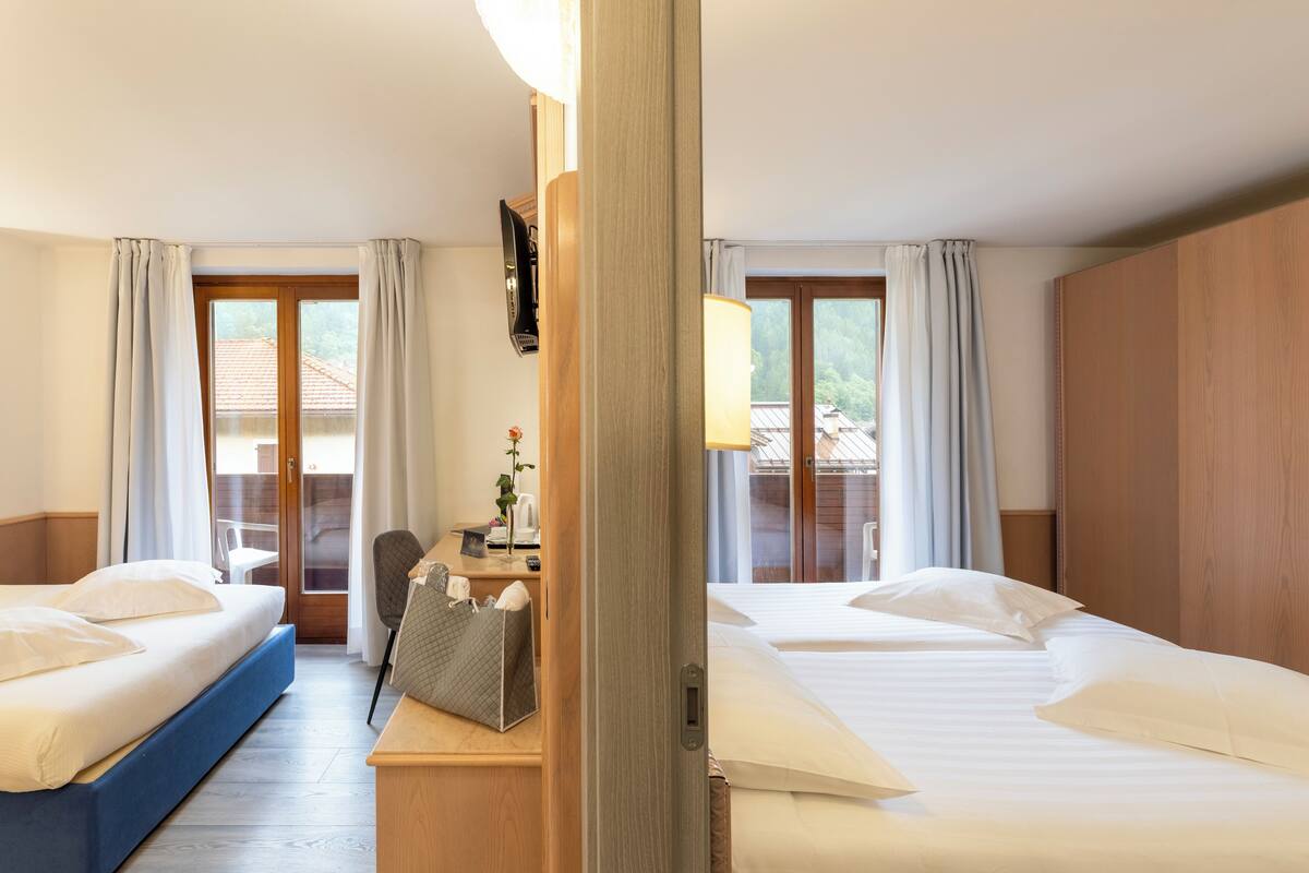 A hotel room with two beds, a desk, a chair, and a view of the outside.