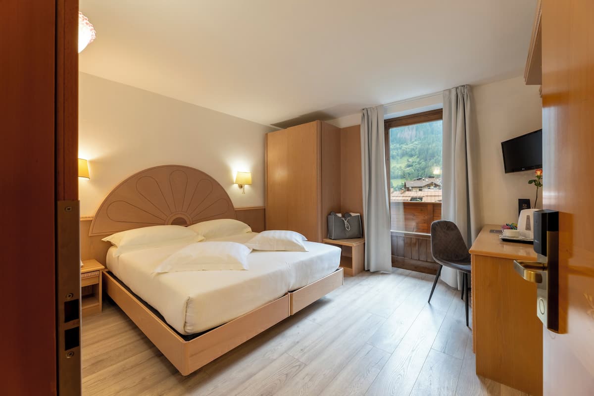 A hotel room with a bed, desk, chair, TV, and a view of the outdoors.