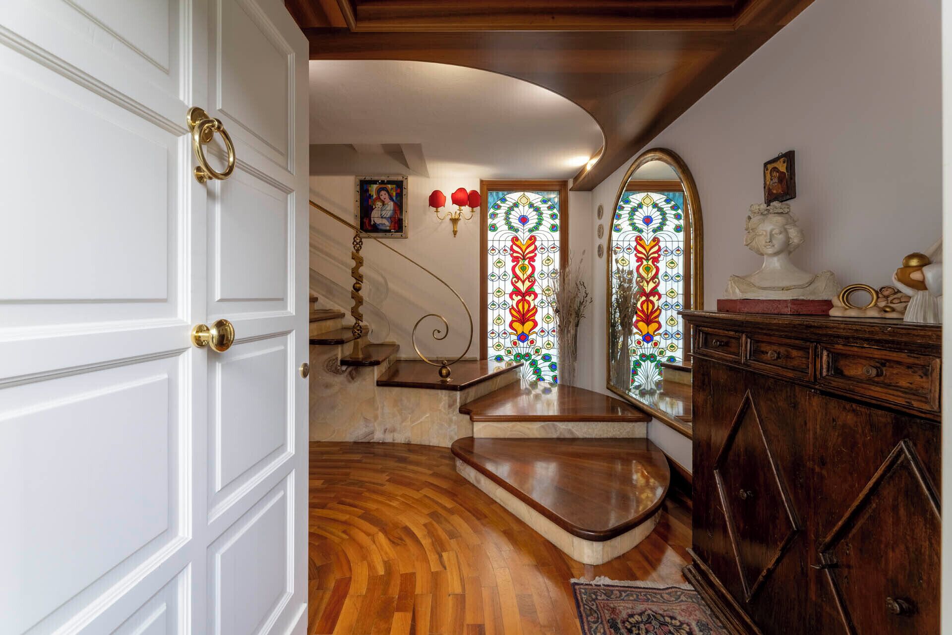 A grand staircase with a marble floor, leading to a room with a wooden ceiling and a large mirror.