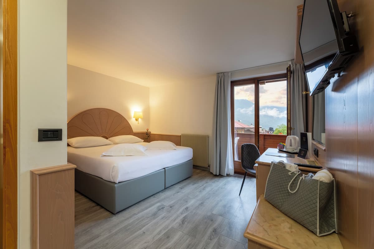 A hotel room with a bed, a desk, a chair, a TV, and a view of the outdoors.