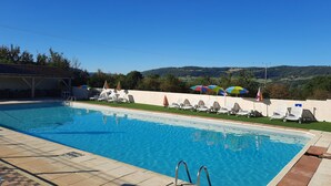 Une piscine entourée de chaises longues et de parasols, le tout bordé d’un mur blanc et offrant une vue sur des collines.