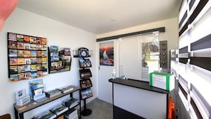 Un espace d’accueil comprenant un comptoir, un panneau d’affichage avec des cartes postales, un tableau encadré et un panneau de commande fixé au mur.