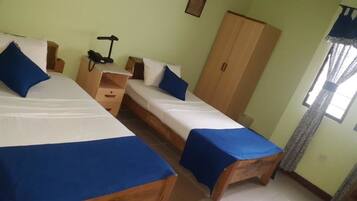 A room with two beds, a wardrobe, a desk with a lamp, and a window with curtains.